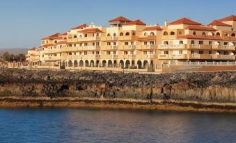 a large building with a red roof is situated on the edge of a body of water at Elba Castillo San Jorge & Antigua Suite Hotel