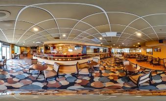 a panoramic view of a modern bar with wooden chairs , a curved ceiling , and large windows at Chester Hotel and Conference Center