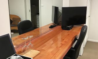 a wooden desk with two computer monitors and a wine glass on it , reflecting in a large mirror at Black Forest Motel