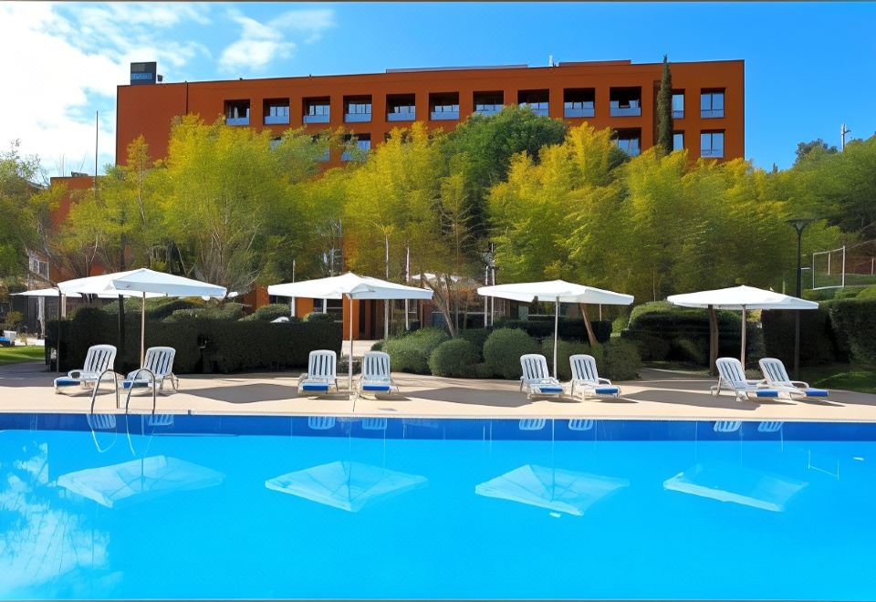 a large swimming pool surrounded by lounge chairs and umbrellas , with a building in the background at Abba Garden