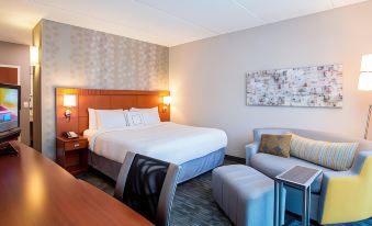 a modern hotel room with a large bed , white linens , and a comfortable living area at Courtyard Rochester Brighton