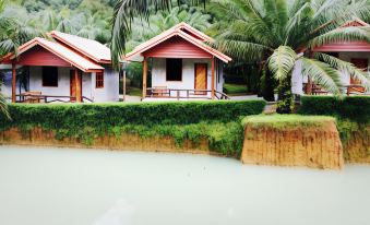 two small wooden houses situated next to a body of water , surrounded by lush greenery at Palmsuay Resort