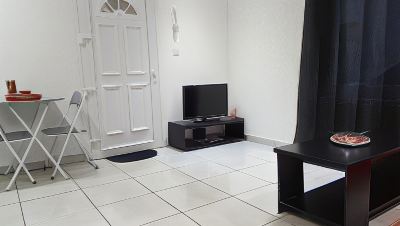 a small living room with a tv on a stand , black and white tiles on the floor , and white doors at Vichy