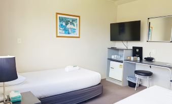 a hotel room with a bed , desk , and tv , along with white walls and gray carpet at Auckland Airport Motel