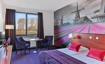 a modern hotel room with a large bed , two chairs , and a window overlooking a windmill field at Fletcher Hotel-Restaurant Zevenbergen-Moerdijk