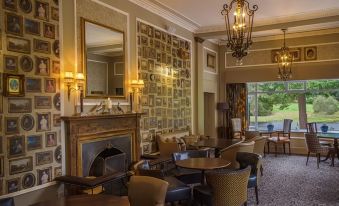 a room with a fireplace , chandeliers , and chairs arranged around tables filled with people at Banchory Lodge Hotel
