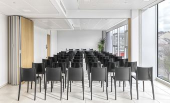 a large , empty conference room with rows of black chairs and a blank white screen at Noa Boutique Hotel