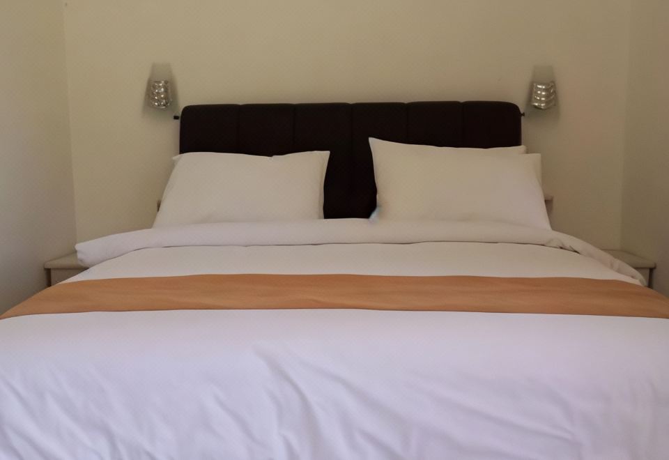 a neatly made bed with white sheets and two pillows , set against a beige wall at Sacca Residence & Resto