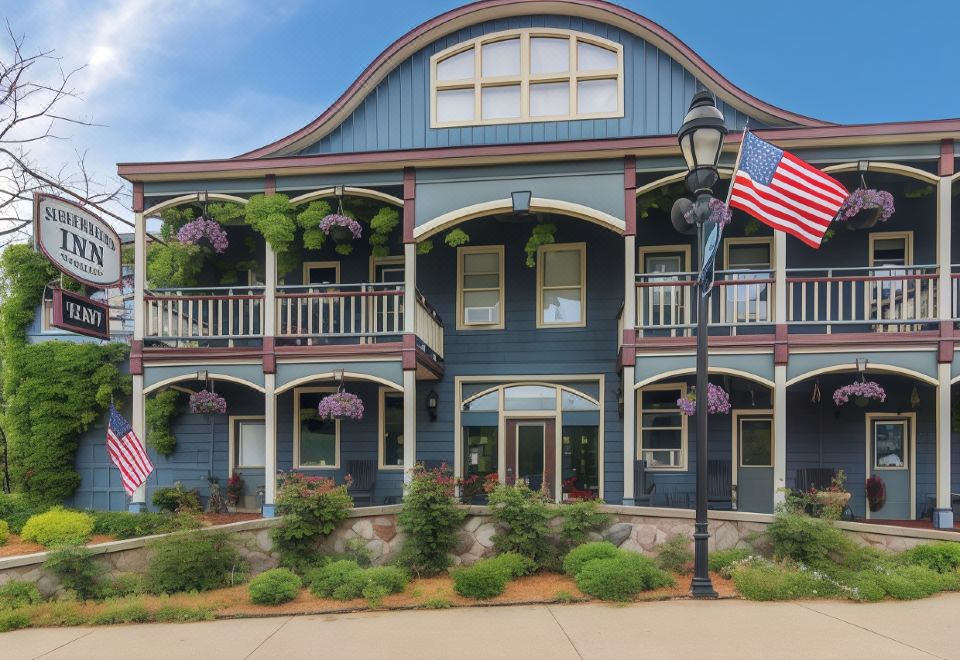 a blue and white two - story building with a flag flying on top , surrounded by trees and flowers at Stone Waters Inn