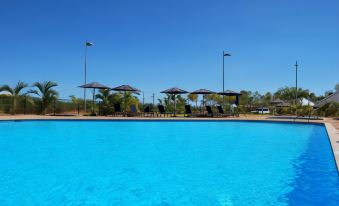 a large outdoor swimming pool surrounded by lounge chairs and umbrellas , providing a relaxing atmosphere at Exmouth Escape Resort