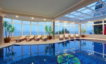 a large indoor swimming pool surrounded by lounge chairs , with a view of the ocean in the background at Hotel Savoy