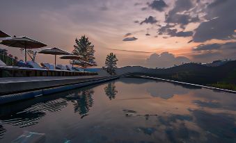 a tranquil pool area with umbrellas and chairs , set against the backdrop of a beautiful sunset at Santani Wellness Kandy