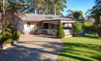 a house with a sloping roof and large windows is surrounded by greenery and has a patio area with potted plants at Fairway Motor Inn