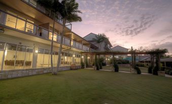 a large building with a grassy area and palm trees in front of it at sunset at Mercure Clear Mountain Lodge