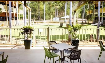 an outdoor dining area with a table and chairs , surrounded by potted plants and grass at Litchfield Outback Resort