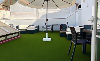 an outdoor dining area with a green carpet , white table and chairs , and an umbrella at La Torre