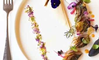 a white plate with a fish and a fork on it , along with some vegetables and flowers at Logis la Résidence
