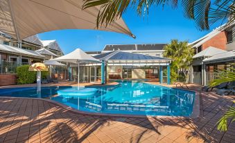 a large swimming pool with a covered area and palm trees in front of it at Broadwater Resort Como