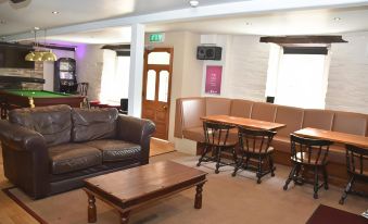 a modern living room with a couch , coffee table , and dining area features brown leather seats and wooden tables at The Red Lion