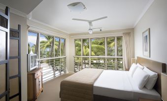a spacious bedroom with a large bed , a tv , and a view of palm trees outside the window at Mantra Amphora