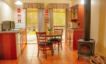 a cozy kitchen with a dining table and chairs , a stove , and a window overlooking the outdoors at Kalimna Woods Cottages