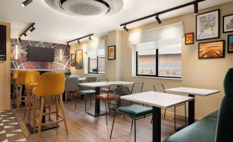 a modern restaurant with white tables and chairs , green chairs , and wooden floors , under a large circular light fixture at Super 8 by Wyndham Chester East