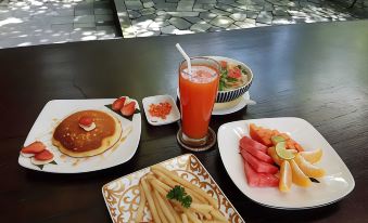 a table with plates of food and a glass of juice , including a burger , fries , and watermelon slices at Rumah Batu Boutique Hotel