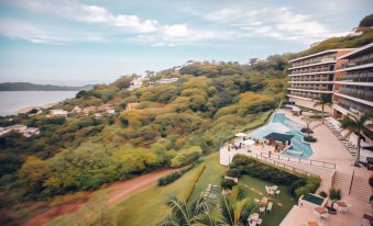 a large hotel is situated on a cliff overlooking a pool and the ocean , with people enjoying their time there at Wyndham Tamarindo