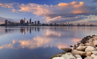 a serene view of a city skyline reflected in the water , with some birds perched on a rock near the shore at Swan River Hotel