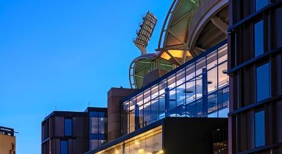 a modern building with a unique architectural design , including a large glass structure and a blue building exterior at Oval Hotel at Adelaide Oval, an EVT hotel