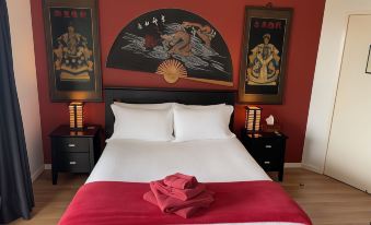 a large bed with a red blanket and white sheets is in a room with two paintings on the wall at Tambaridge Bed & Breakfast