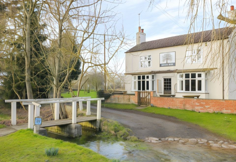 a white house with a green lawn and trees , next to a small pond and a small bridge at The Barn