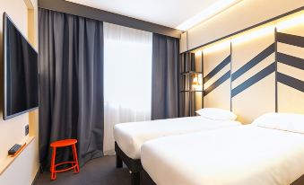 a modern hotel room with two beds , a window , and a red stool near the window at Ibis Styles Geneve Palexpo Aeroport