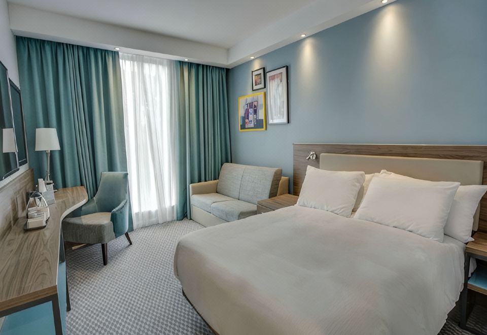 a modern hotel room with blue walls , white bedding , and a comfortable bed , along with a window and couch at Hampton by Hilton Edinburgh Airport