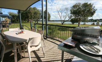 a patio with a table , chairs , and a grill overlooks a lake and trees from a balcony at Discovery Parks - Ballina