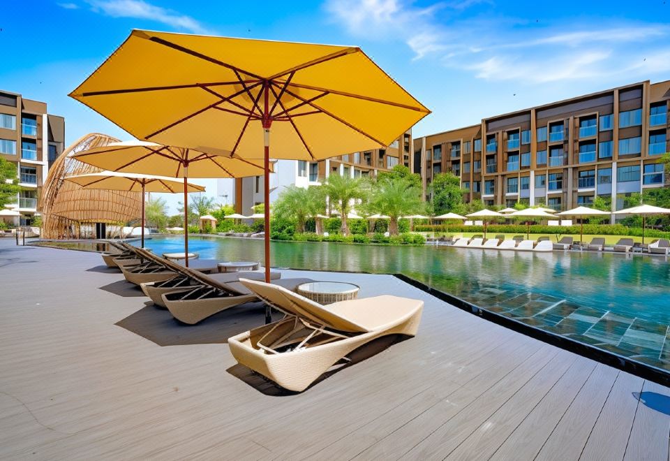 a large swimming pool surrounded by lounge chairs and umbrellas , providing a relaxing environment for guests at Divalux Resort and Spa Bangkok, Suvarnabhumi Airport-Free Shuttle