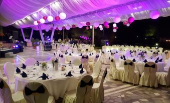 a large banquet hall filled with numerous tables and chairs , decorated with white tablecloths and centerpieces , under purple and pink lighting at Hotel Bellevue