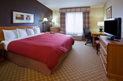 a large bed with a red comforter is in the center of a hotel room with a window , chair , desk , and lamp at Country Inn & Suites by Radisson, Watertown, SD