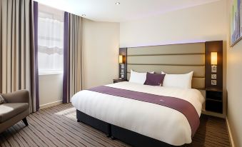 a large bed with white and purple linens is in a room with a window at Premier Inn Melton Mowbray