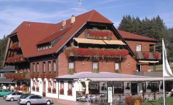 a large red building with white walls and windows , surrounded by trees and parked cars at Hotel Faller