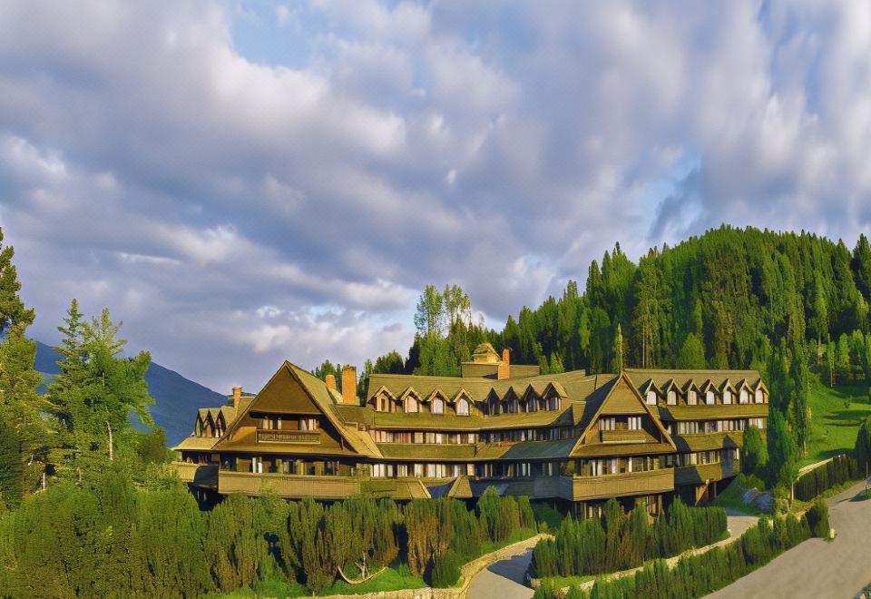 a large wooden building surrounded by trees and mountains , with a cloudy sky in the background at Trapp Family Lodge