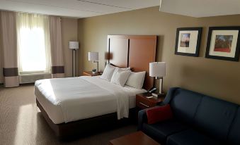 a large bed with white sheets is in a hotel room next to a couch and desk at Wingate by Wyndham Clearfield