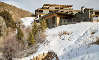 a modern house is perched on a snowy hillside , with snow - covered trees and mountains in the background at The Lodge at Blue Sky, Auberge Resorts Collection