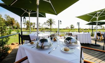 an outdoor dining area with a table set for two people , surrounded by lush greenery and a beautiful view of the surrounding area at Tikida Golf Palace
