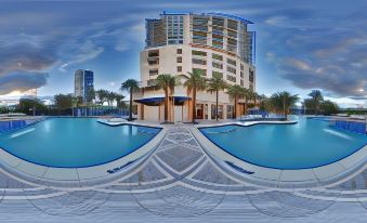 a large pool is surrounded by a resort building and palm trees , with a blue sky in the background at Marriott's Oceana Palms