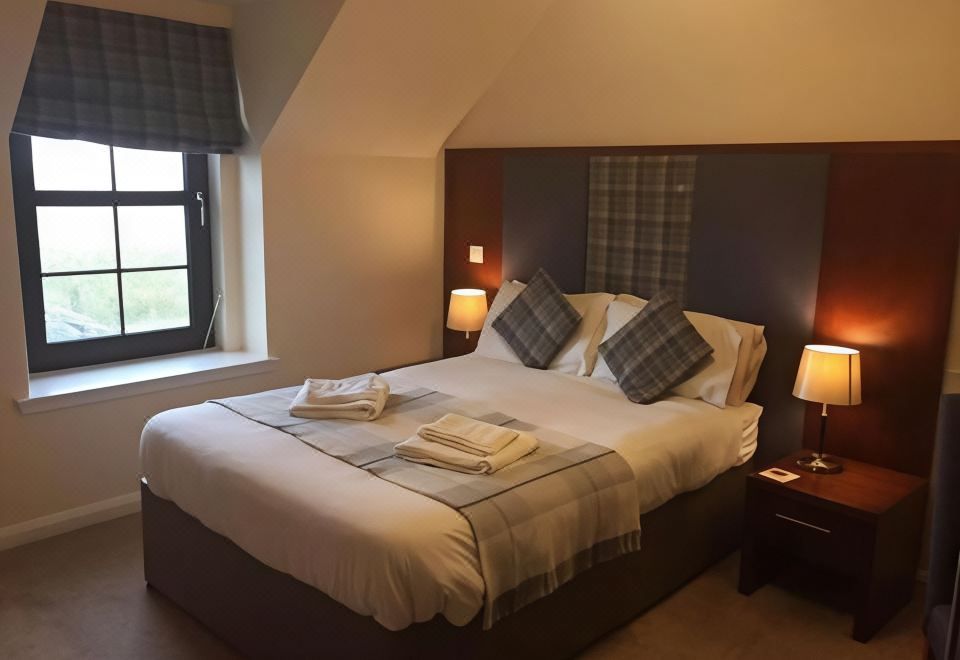 a large bed with a white comforter and pillows is situated in a room with a window at Polochar Inn