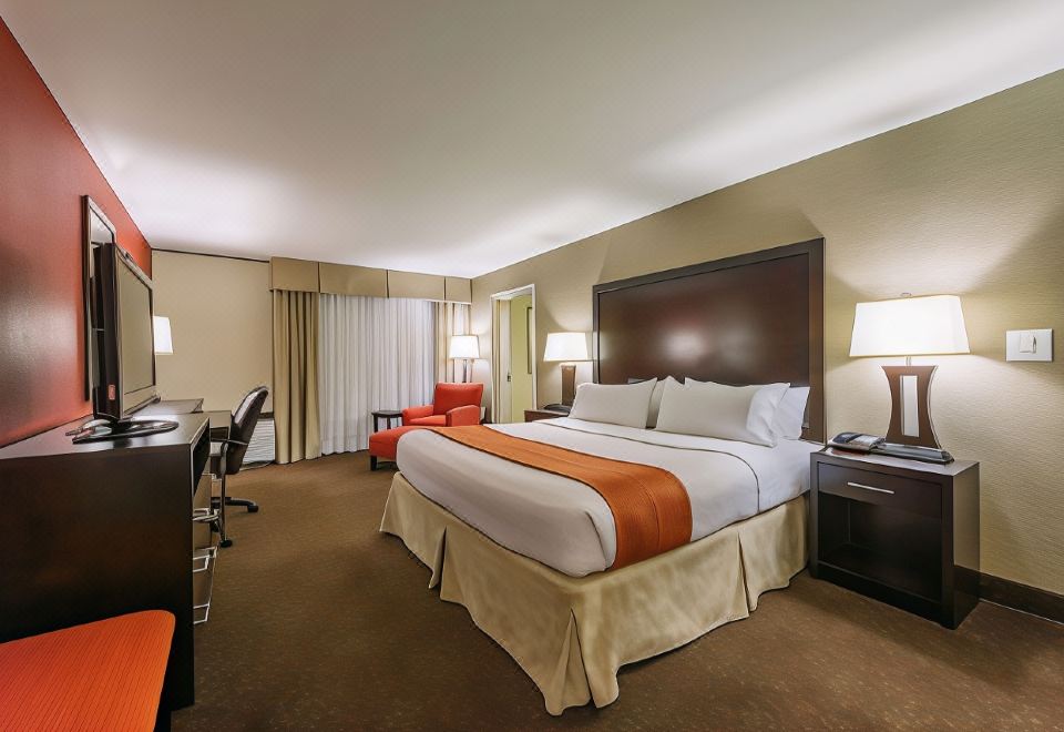 a large bed with a brown headboard and orange blanket is in the middle of a hotel room at Hotel Mtk Mount Kisco