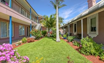 a large lawn with a palm tree and several buildings in the background , creating a tropical atmosphere at Shellharbour Village Motel