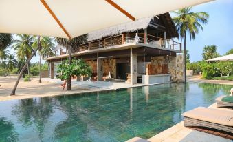 a large swimming pool is surrounded by lounge chairs and a thatched roof house with palm trees in the background at Karpaha Sands