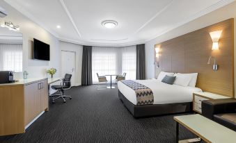 a large bed with a headboard and footboard is in the middle of a room with gray carpeting at Mercure Goulburn